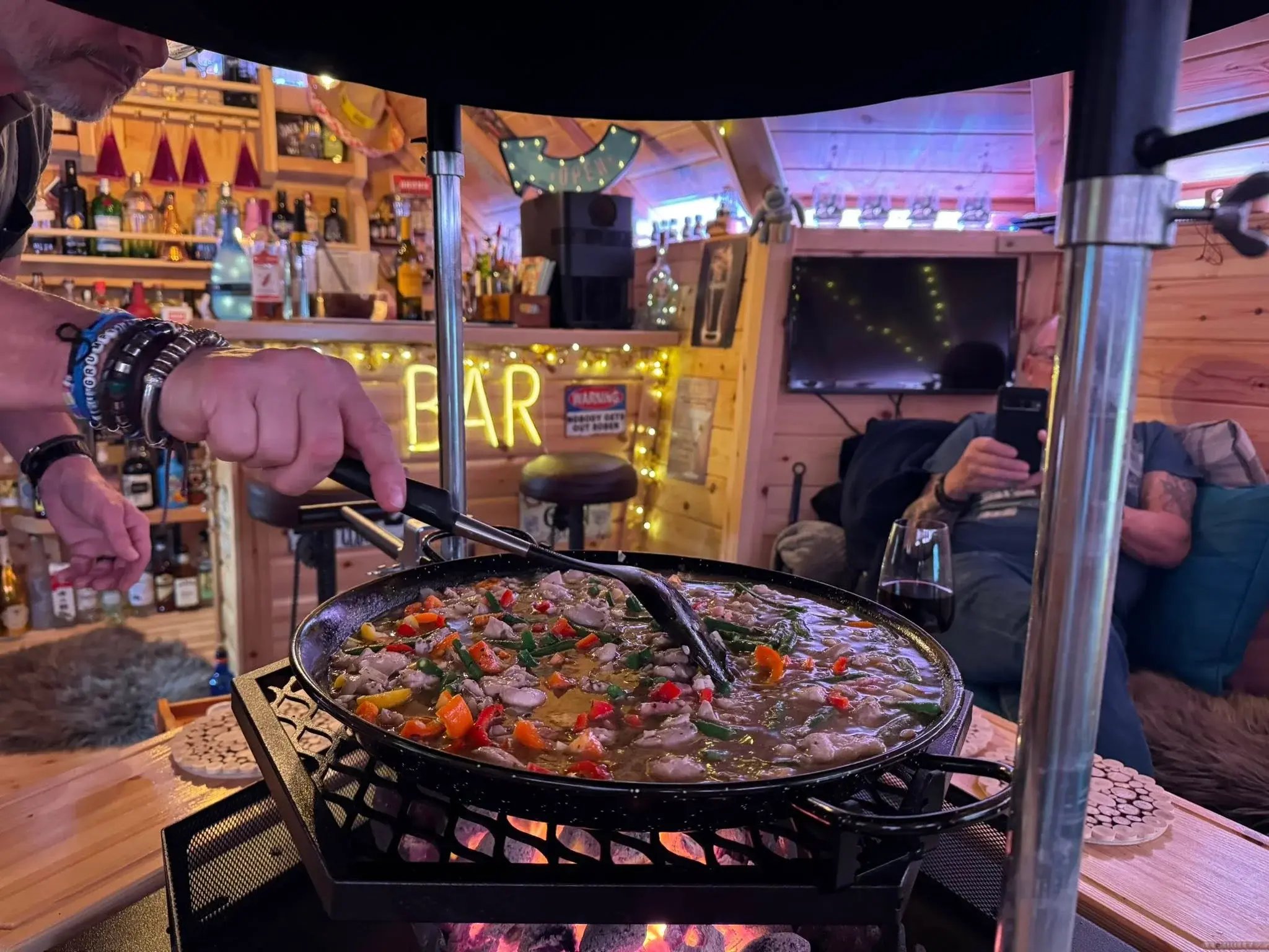 Paella being stirred in a traditional paella pan over a indoor BBQ grill.