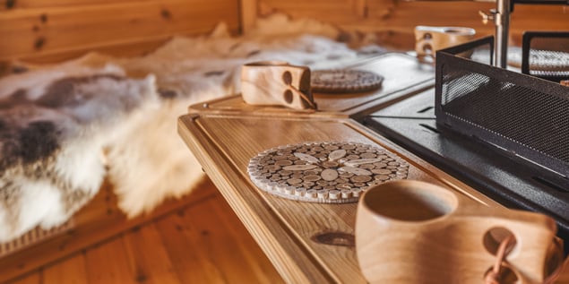 Timber tables with log placemats and wooden cups surrounding the grill of a BBQ cabin