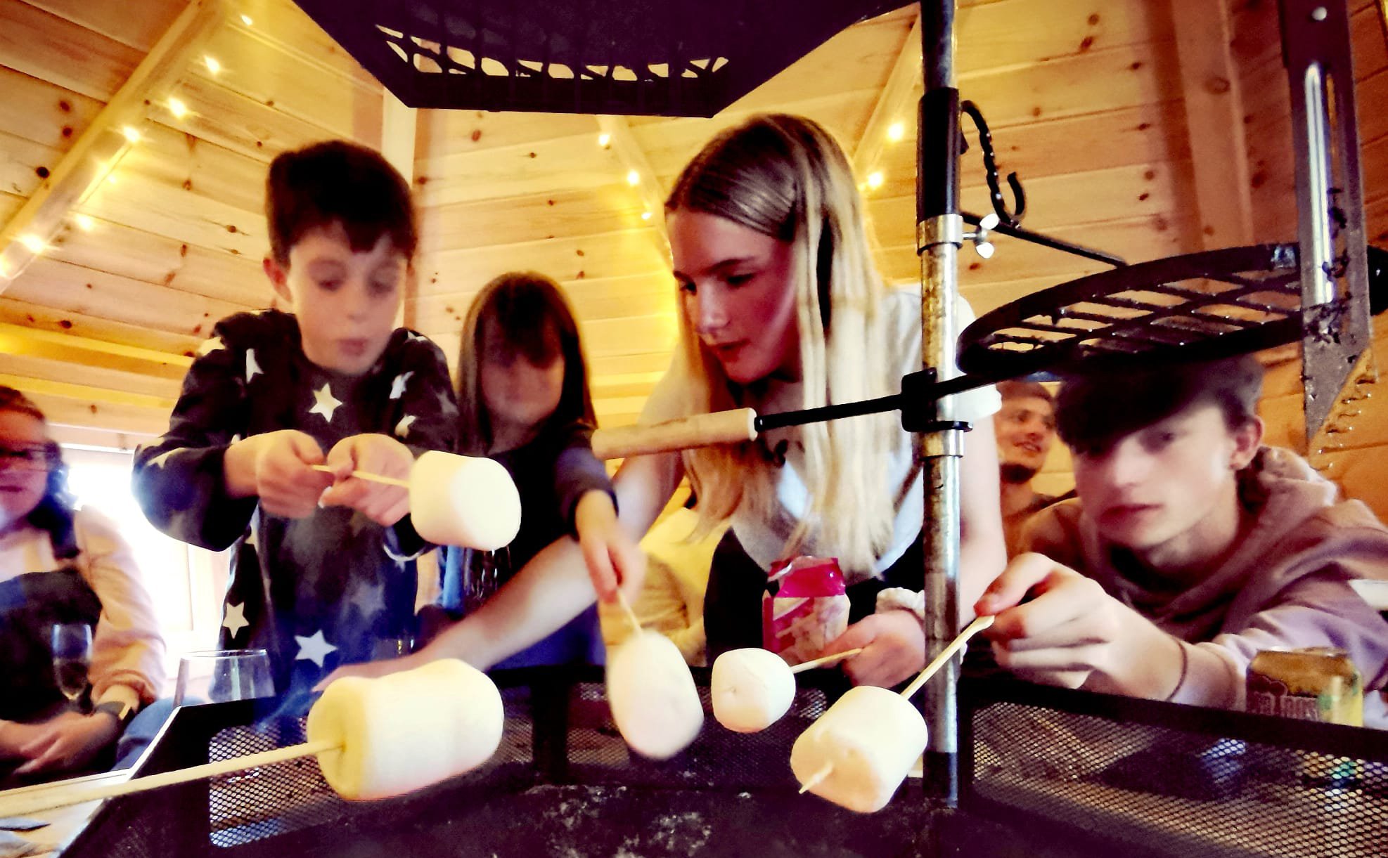 Children roasting marshmallows over the hot coals, inside their Arctic Cabins BBQ hut