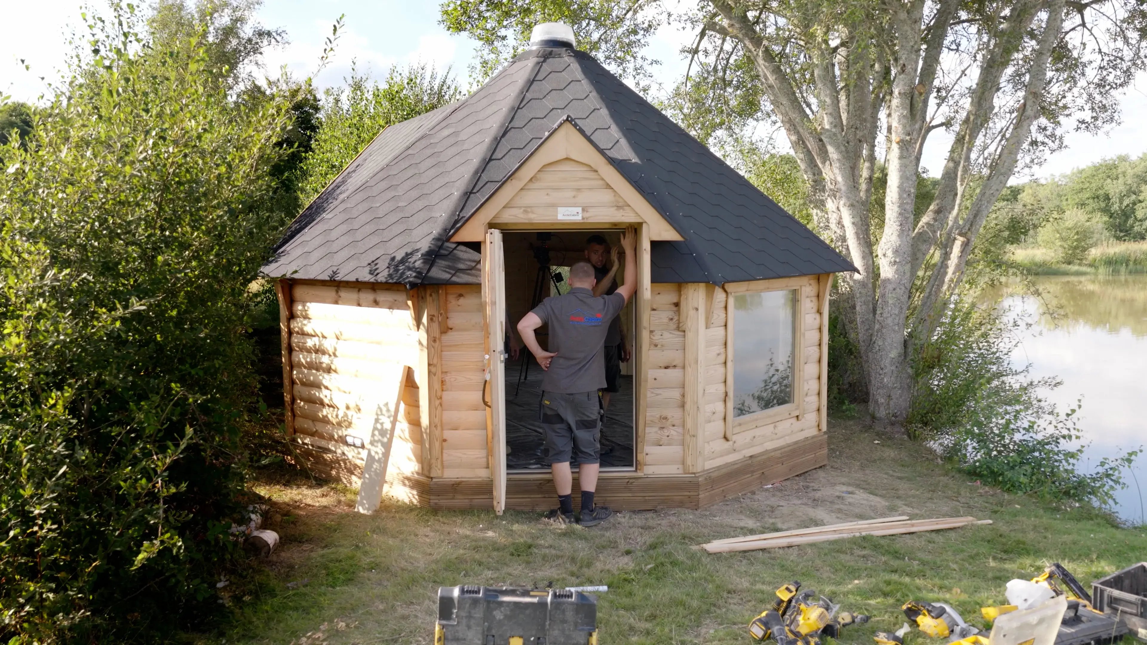 An Arctic Cabins builder stood in the doorway of Vinnie Jones' log cabin. On the grass in front of the cabin there are power tools and a few planks of wood.