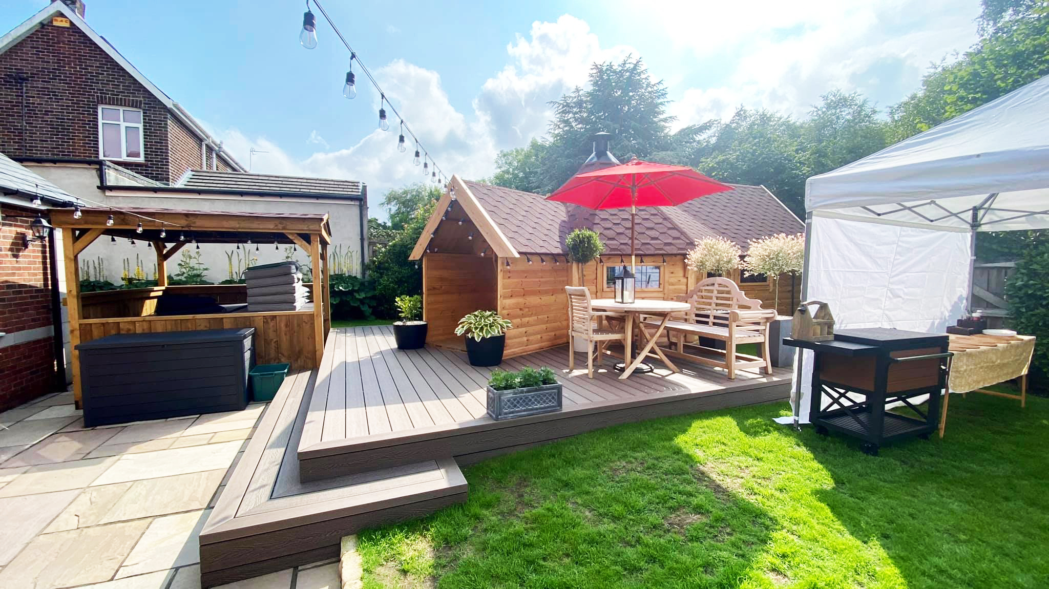 External shot of a BBQ cabin bar on decked area with hanging festoon lights and red parasol